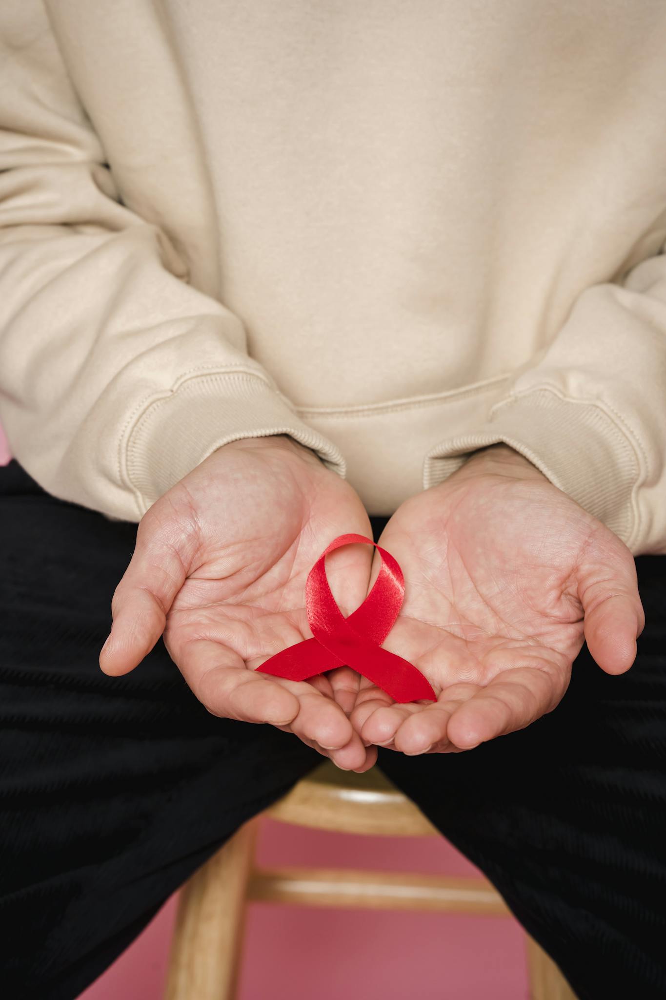 Close-up of hands holding a red ribbon symbolizing AIDS awareness. Promote healthcare support.